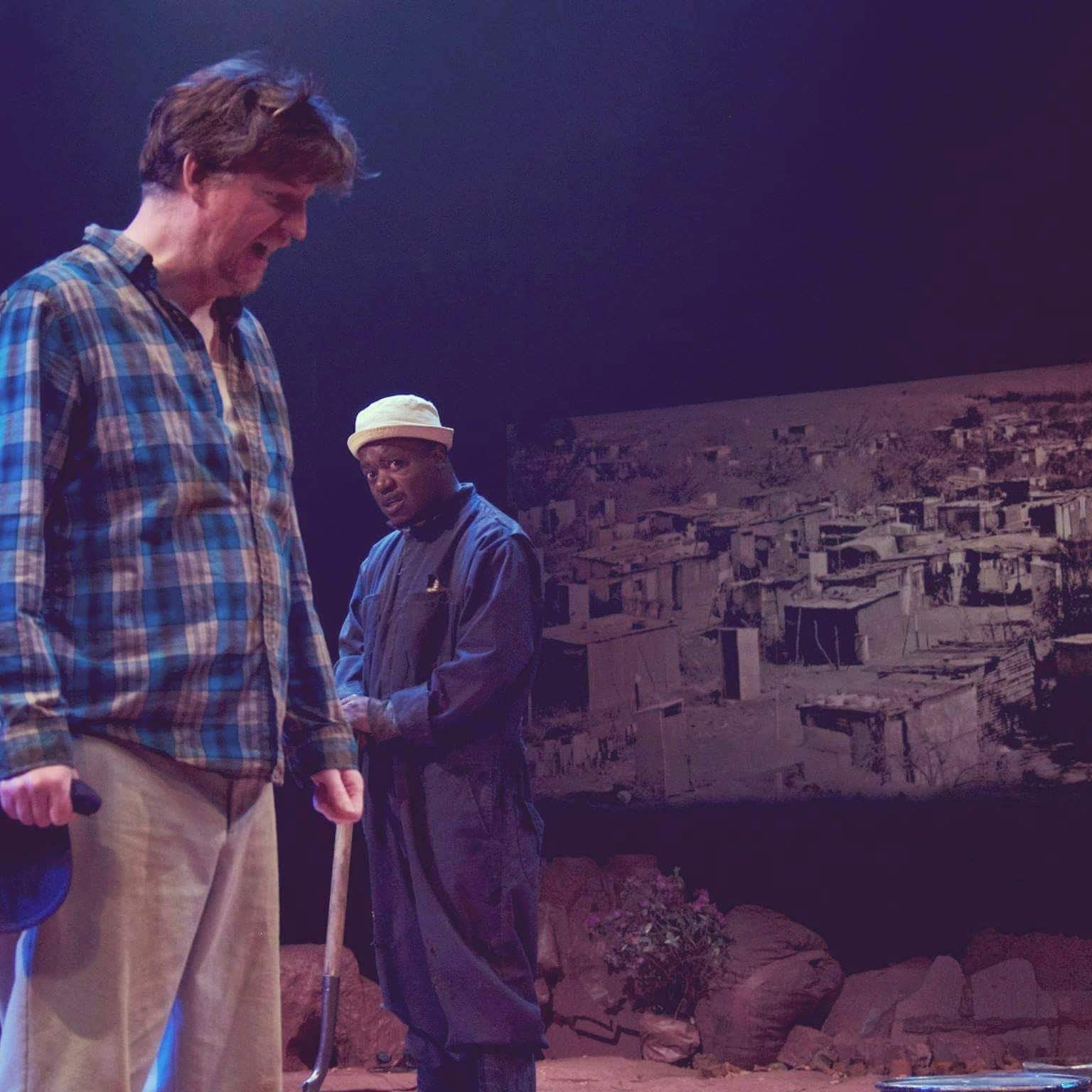 Clayton Pasi Gunguwo holding a shovel on a dusk-lit stage, facing his scene partner